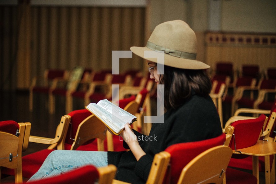 a woman sitting in an empty church reading a Bible 