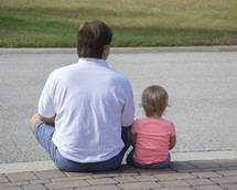a father sitting with his daughter on a curb 