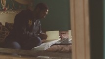 a college student reading a Bible on his bed 