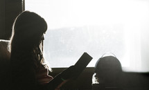 a girl reading a book in a window 
