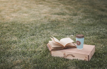 coffee cup with cross on grass with Bible and wood box 