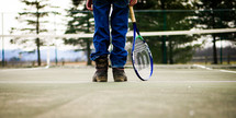 man in jeans standing on a tennis court 