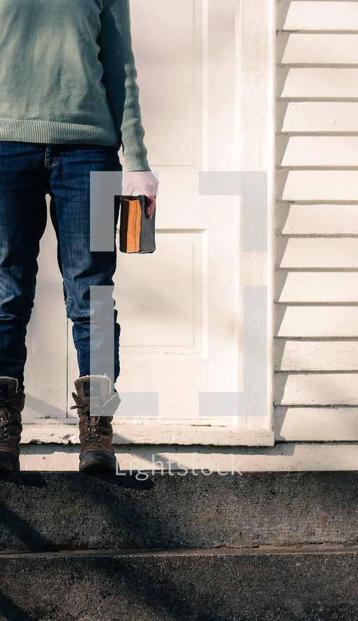 a woman in boots standing on steps holding a Bible in front of a church 