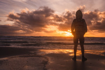 silhouette of a child standing on a shore at sunset 