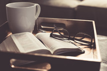 tea cup, open Bible, and reading glasses on a tray 