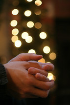 praying hands in front of a Christmas tree