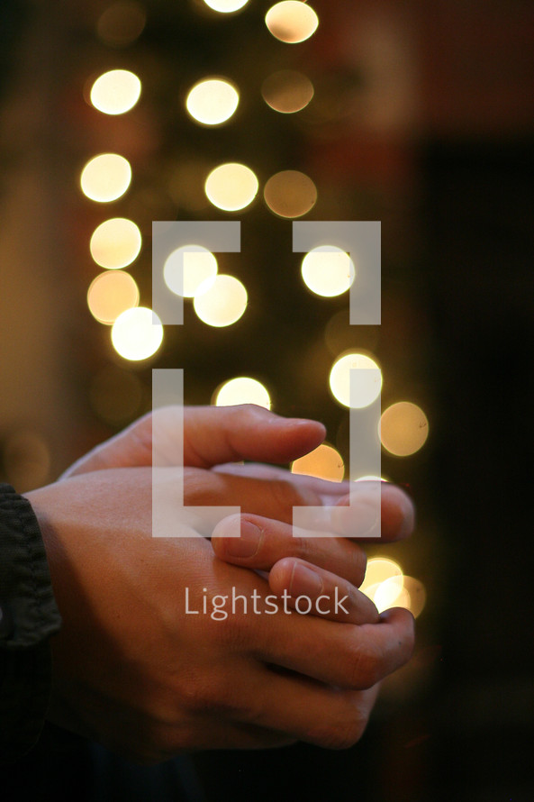 praying hands in front of a Christmas tree
