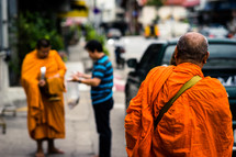 Buddhist monks in orange robes walking on a sidewalk 