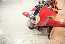 A child sitting in a weathered pedal red airplane .