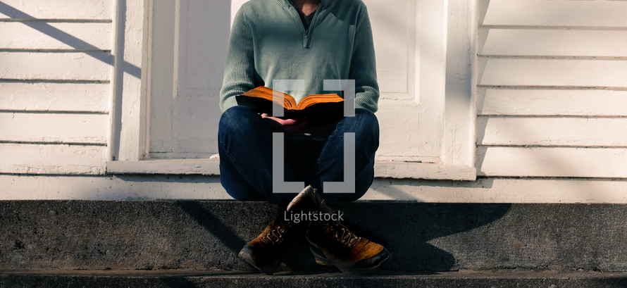 a woman in boots sitting on steps in front of a church holding a Bible 