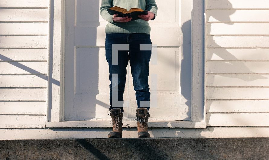 a woman in boots standing on steps in front of a church reading a Bible 