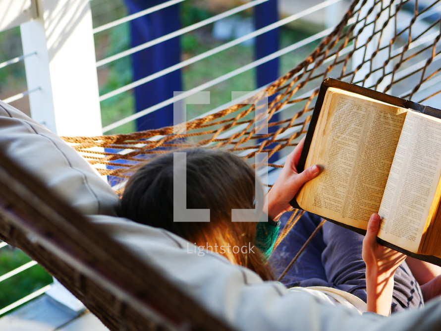 a woman reading a Bible in a hammock 