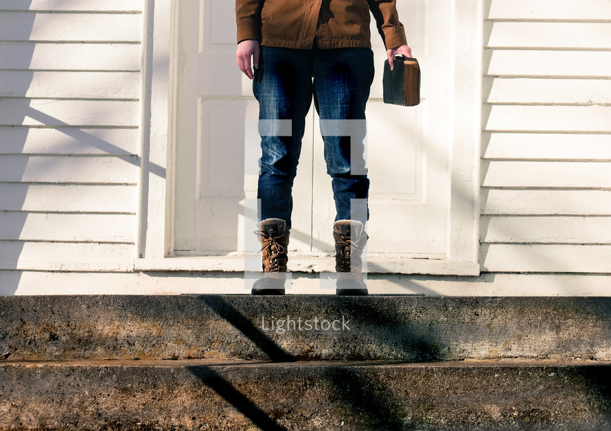 a woman in boots standing on steps in front of a church holding a Bible 