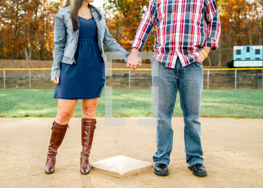 couple holding hands on a baseball field 
