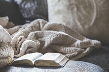 open Bible and blanket on a couch 