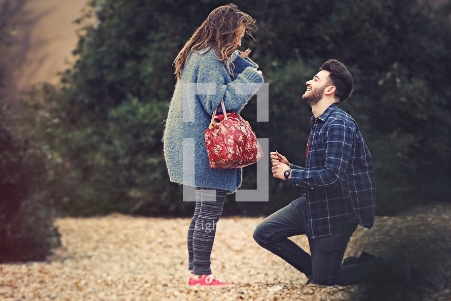 A young man on one knee proposing to a young woman.
