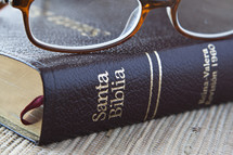Reading glasses resting on Spanish Bible.