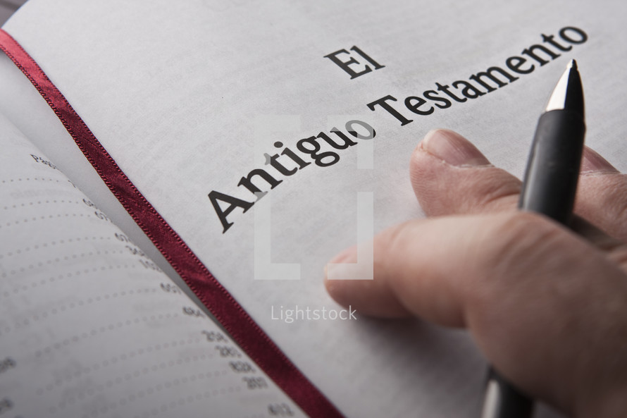 Hand holding pen on Spanish Bible.