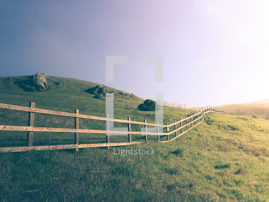 Wooden fence in the grass over rolling hills.
