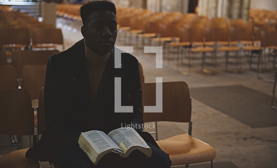 African American man sitting in an empty church reading a Bible 