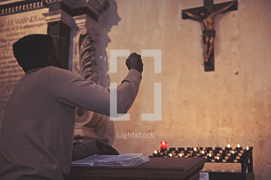 man in prayer in front of prayer candles in a catholic church 
