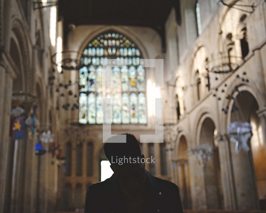 man with head bowed in prayer sitting in an empty church 