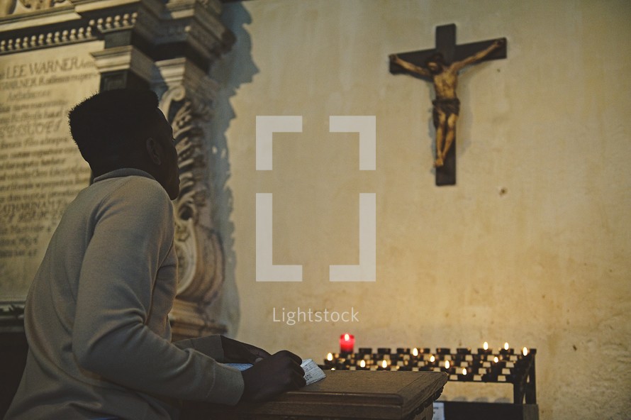 man reading a Bible in front of prayer candles 