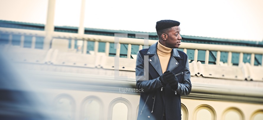 African American man in a leather jacket standing in front of a building outdoors 