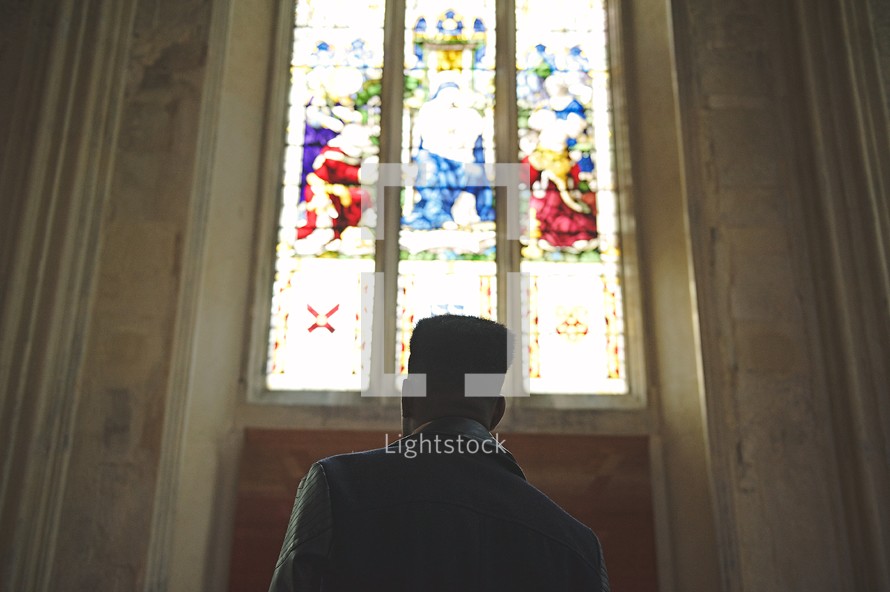 man standing in front of stained glass windows in a church 