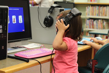 A small girl interacts with a computer at a public library.