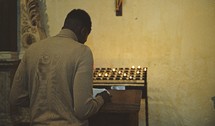 A man reading a Bible in a church and prayer candles 