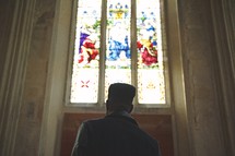 man standing in front of stained glass windows in a church 