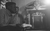 man at a pulpit in prayer holding a Bible 