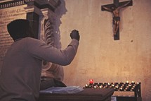 man in prayer in front of prayer candles in a catholic church 