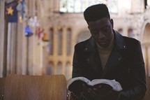 man sitting in an empty church reading a Bible 