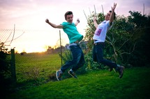 Two boys jumping in the grass at sunset.