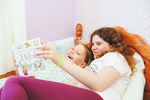 sisters reading a Bible in a bed 