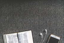 open Bible, earbuds, and cellphone on a couch 
