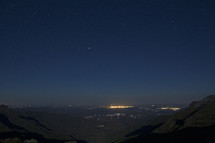 view of lights from a distant city at night standing a the top of a mountain 