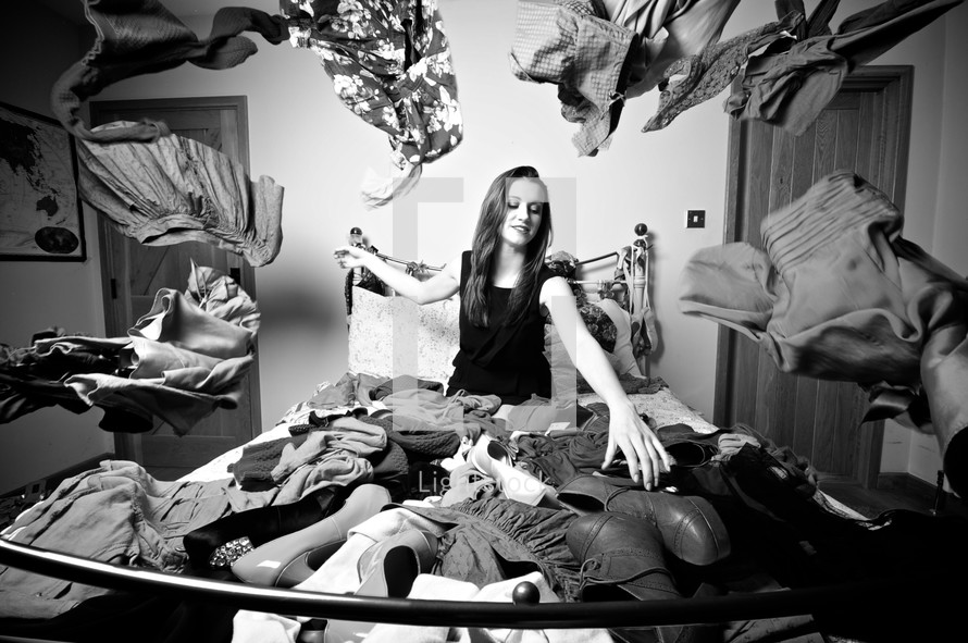 woman sitting on a bed covered in clothes and shoes