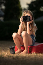 a child holding a camera sitting on luggage 