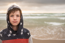 a boy standing on a beach in a hoodie 