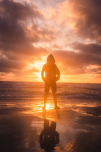 silhouette of a boy standing on a beach at sunset 