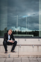 businessman sitting listening to earbuds with reflection of a cloudy sky in the window behind him 