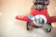 A child sitting in a weathered pedal red airplane.
