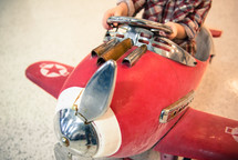 A child sitting in a weathered pedal red airplane.