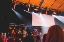 lyrics on a projection screen and worship leaders singing on stage 