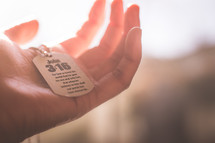 A hand holding a dog tag with John 3:16. 