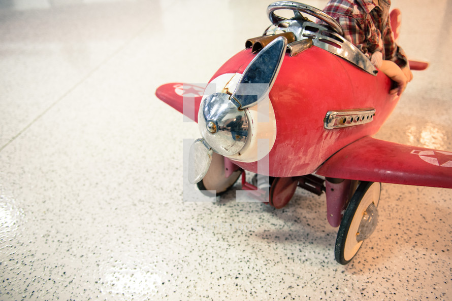 A child sitting in a weathered pedal red airplane .