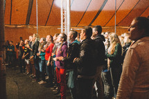 people standing and singing under a tent 